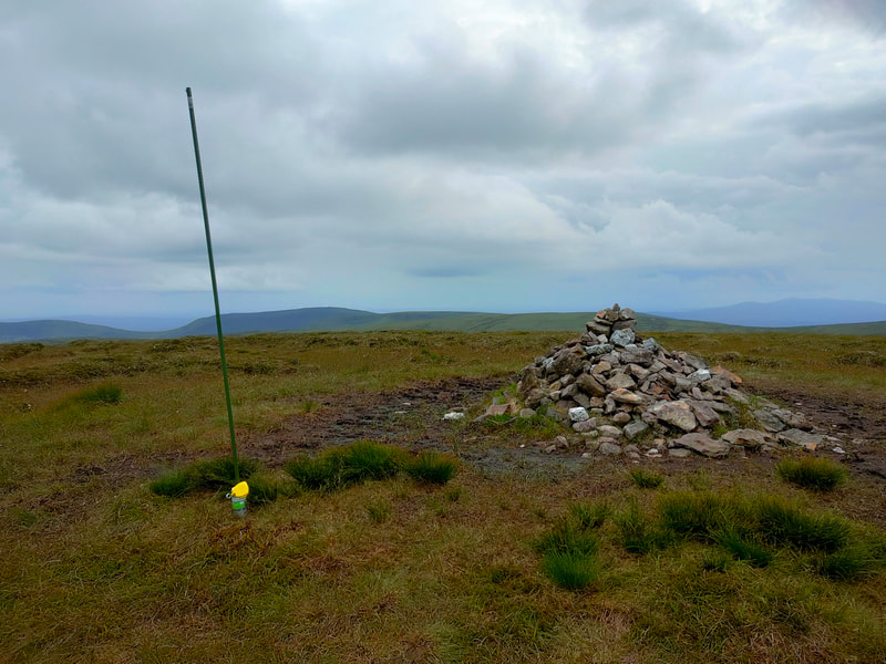 Small pile of stones on a boggy Kilclooney Mountain top with thin green pole