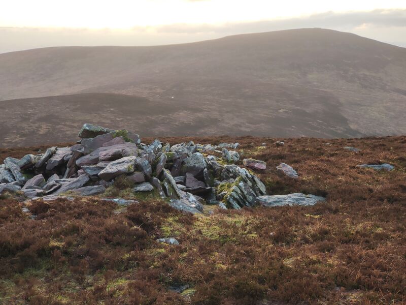 Cairn of stones on top of Knocknalougha mountain with other mountains in the background