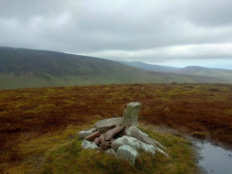 Brown and wet with surface water, the top of Monabrack with a few stones as a mark, other Galty mountains in the background