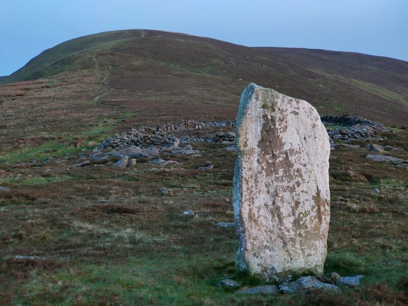 White standing stone and old sheep pen (ring of formed by stone walls) in front of mountain