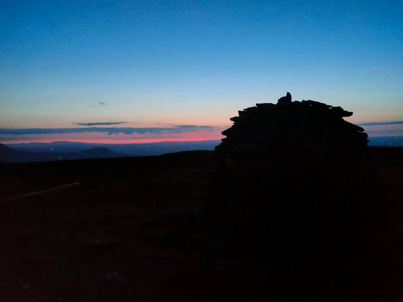 A dark mound of stones marking Musheramore summit with the sky still reddish after sunset