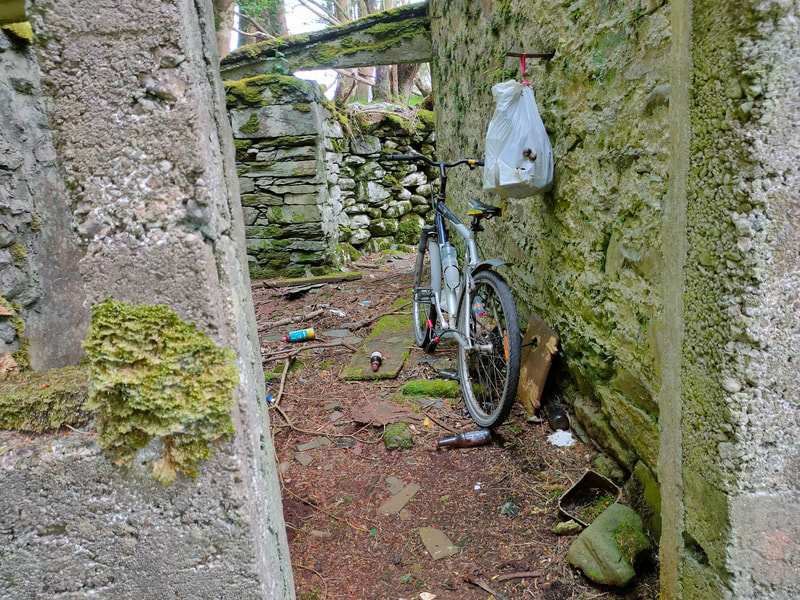 Bicycle standing by wall of old ruin surrounded by some rubbish.