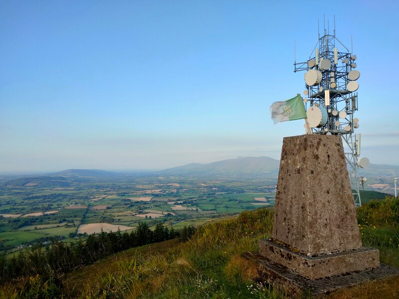 Slievereagh Trig Pillar with communication mast behind and the Galtys against a blue evening sky