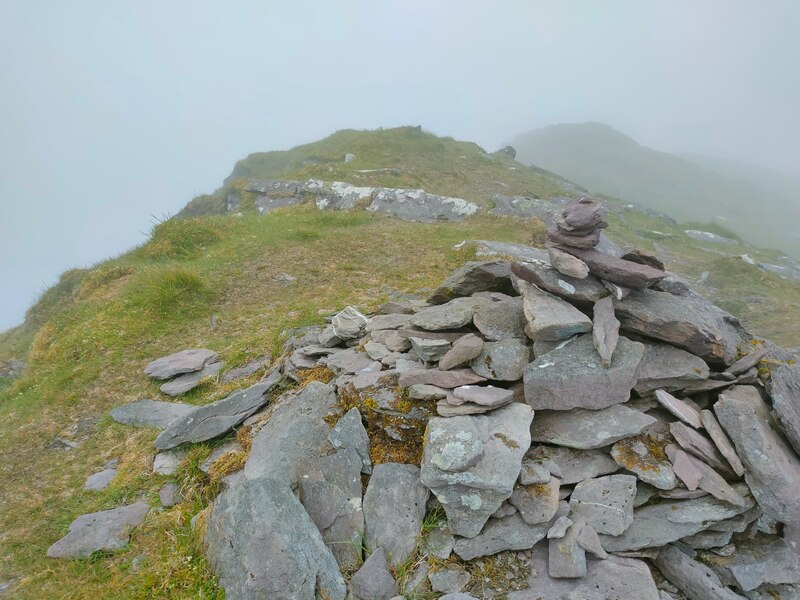 small pile of stones marking the peak of Cnoc an Chuillin, foggy background