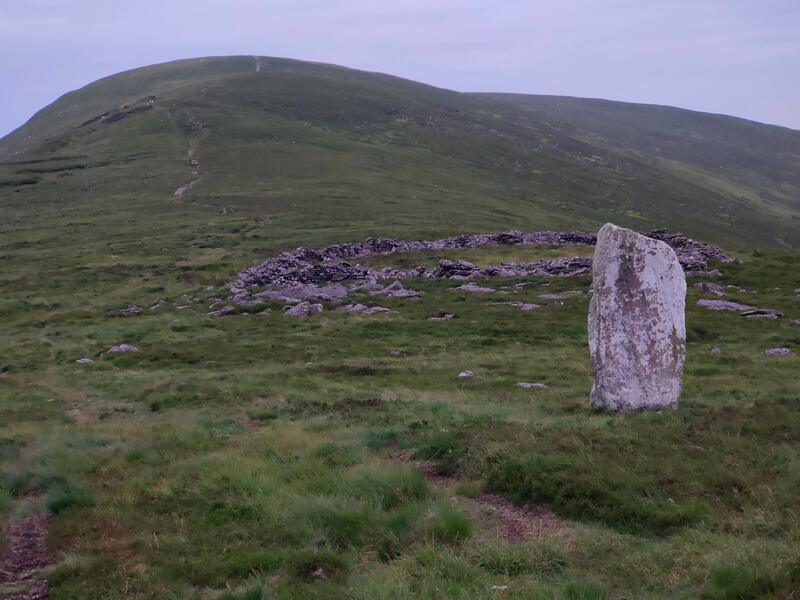White standing stone and old sheep pen (ring of formed by stone walls) in front of mountain