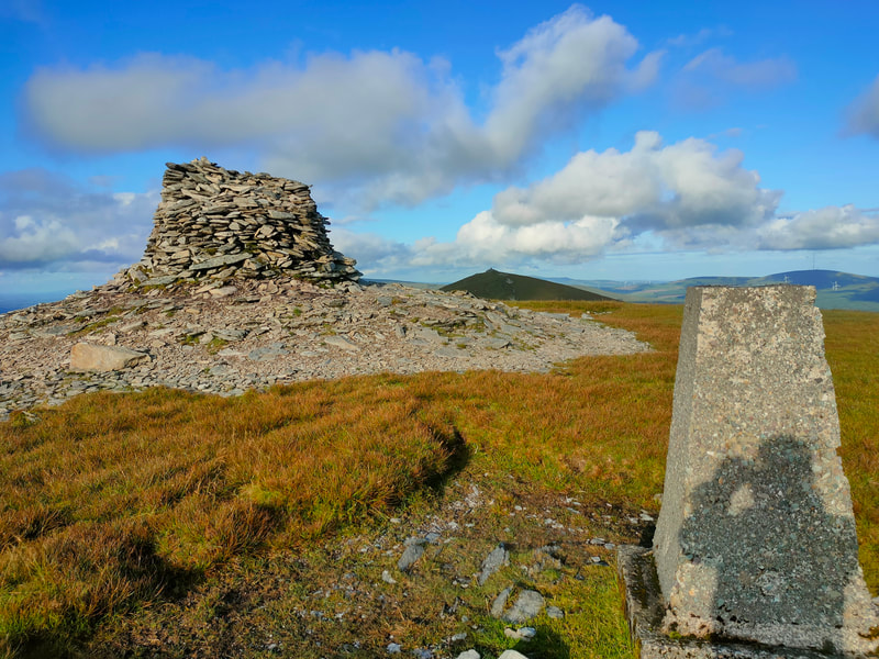 Large pile of stones and Trig Pillar on The Paps West with low evening sunshine