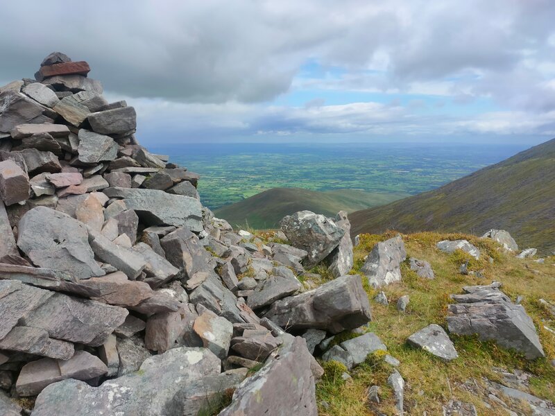 Pile of rocks to mark Cnoc Íochtair with a slight view outwards under cloud