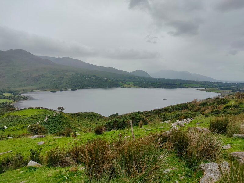Lough Guitane against a grey sky  with green mountain side in the foreground