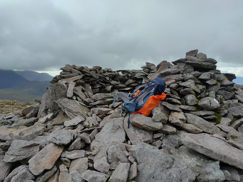Cairn of stones on top of Purple Mountain with black/orange hiking bag on the stones