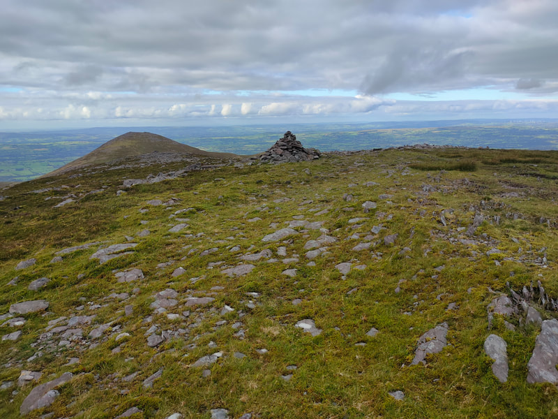 A pointy pile of stones marking Purple Mountain Northeast with Tomies mountain in the distance