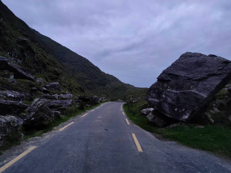 Ballaghbeama Gap, road in the centre of large rocks on one side with rocks rising much higher on the other side.