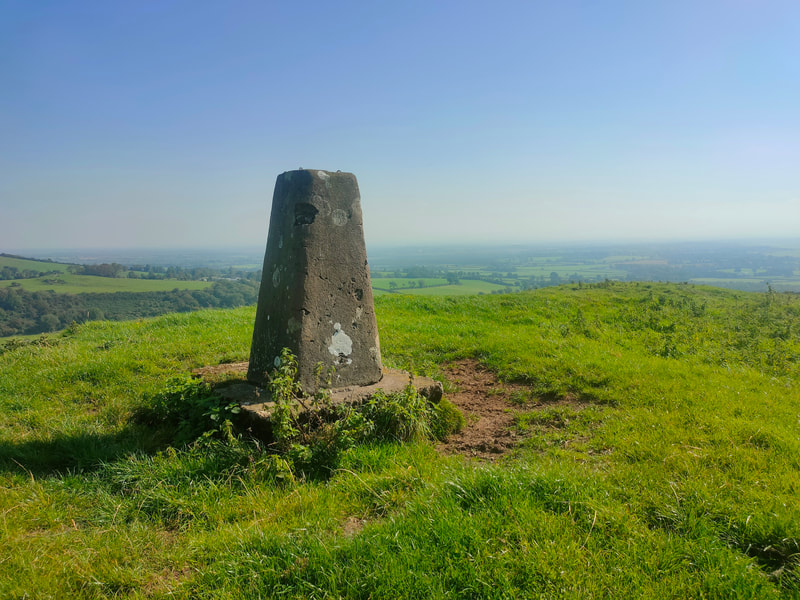 Trig Pillar of Dunmurry Hill on grassy hill top against a blue sky