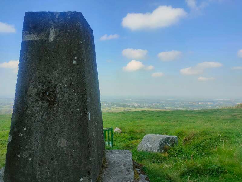 Trig Pillar of Cupidstown Hil looking across a green field and a hazy Kildare beyond.