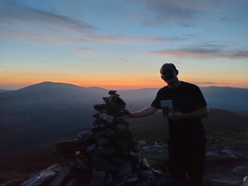 Man standing beside small pile of stones on Scarr mountain after sunset.