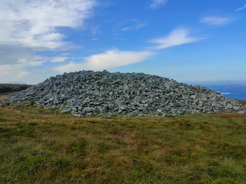 Large cairn of stones on grassy mountain, Blue sky with some white cloud