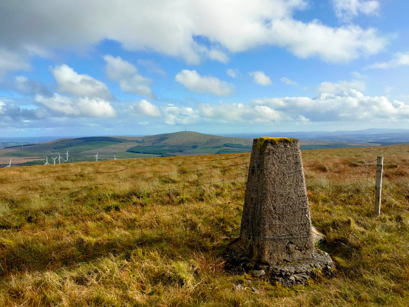 Caherbarnagh Trig Pillar with Mullaghanish in the distance and Blue cloudy sky 