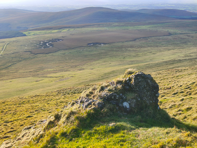 Large rock protruding out of the side of Knocksheegowna with  the bog stretching out below