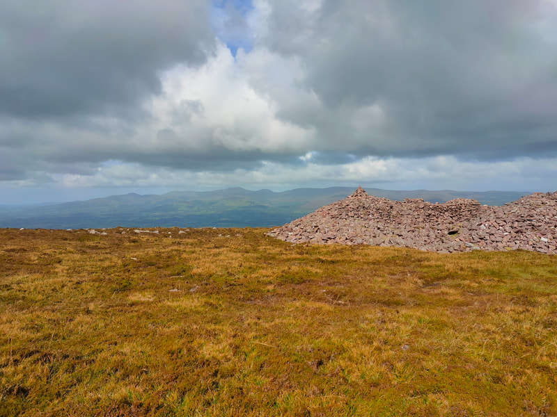 Views of the Galty range of mountains against a grey cloudy sky with Knockahanahullion stone cairn in the foreground