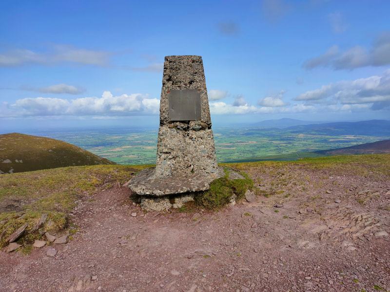 Knockmealdown Trig Pillar and the patchwork of fields in the valley below with Slievenamon on the horizon