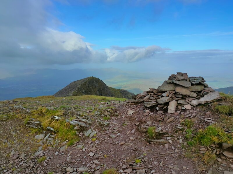 A small pile of stones marks the High Point of Caher with the lower Caher Peak in the distance