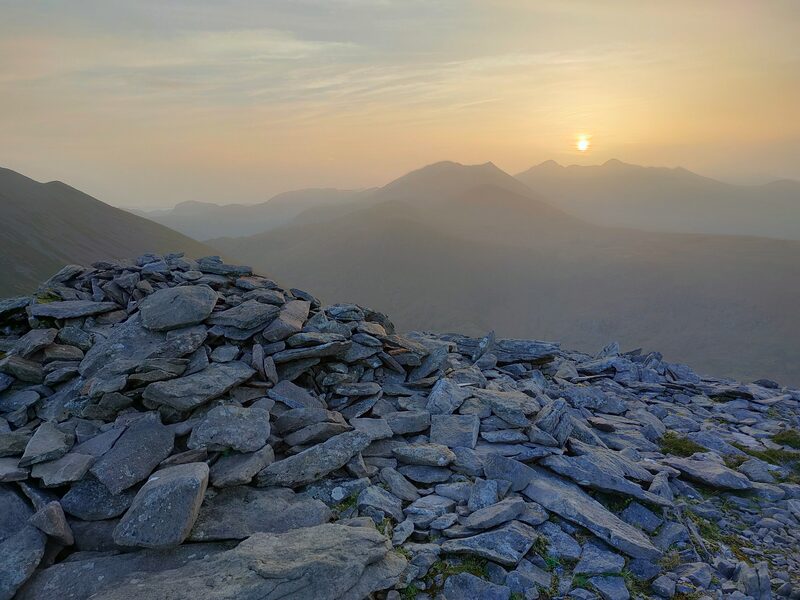 Sunset behind mountains with large pile of stones on the top of Tomies mountain foreground