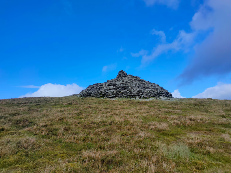 Large mound of stones on the top of The Paps East. Bright blue sky behind.