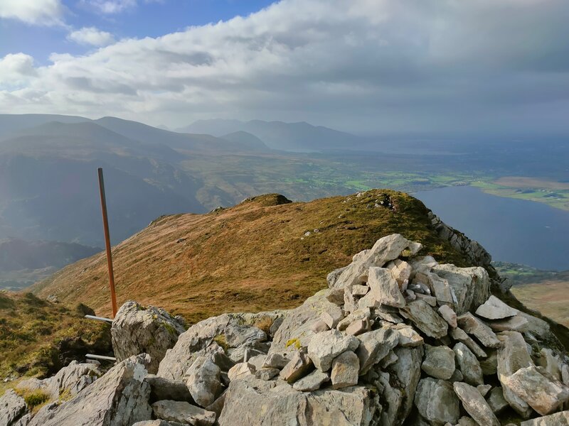 A small pile of stones and Iron bar at the top of ​Crohane with Lough Guitane below