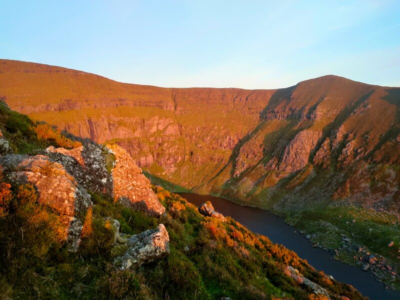 The steep mountain sides of Coumshingaun Lake lit up by the sun