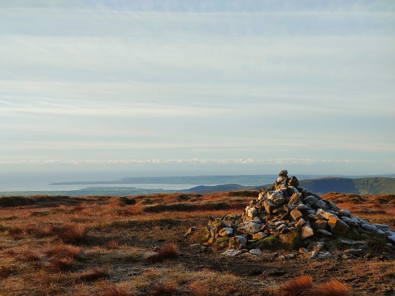 Small mound of stones mark the top of Kilclooney Mountain with Helvic Head in the background.