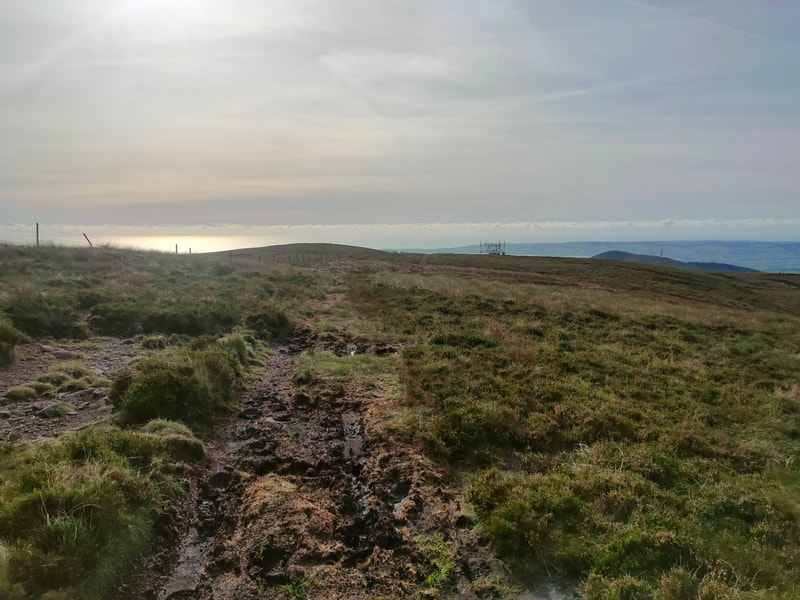 Boggy path leading across a mountain with some communication structures beyond.