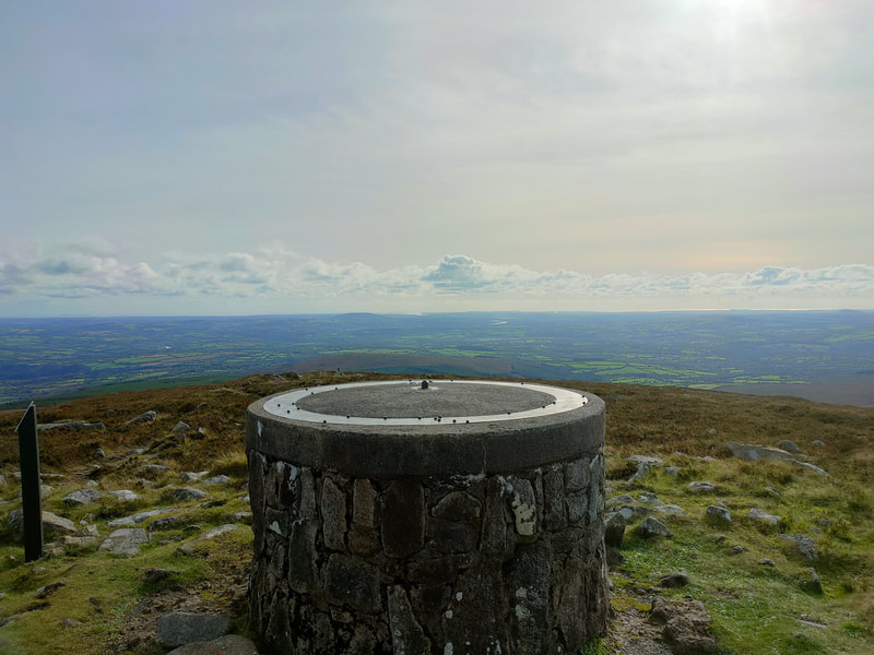 Cylindrical concrete and stone structure with information plate on top. Countryside views to the coast.