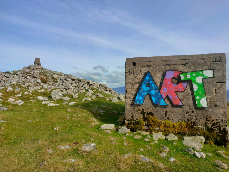Trig Pillar on stone cairn and colourful grafitti, Blue "A", Red "R"and Green "T" on small cube shaped building