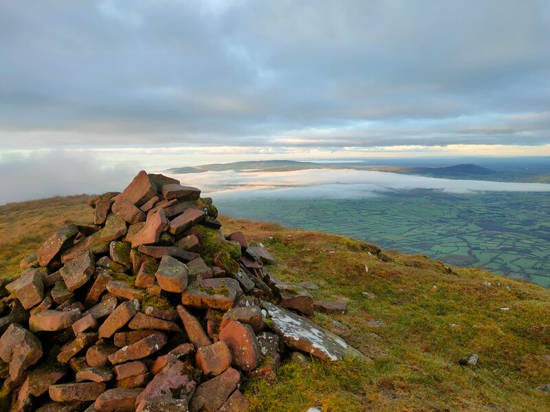 A pile of stones marking Lyracappul with farmland and cloud inversion below