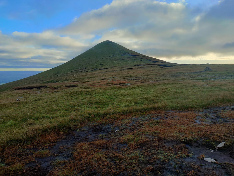 Wet boggy mountain surface with peak rising into the white cloudy and blue sky