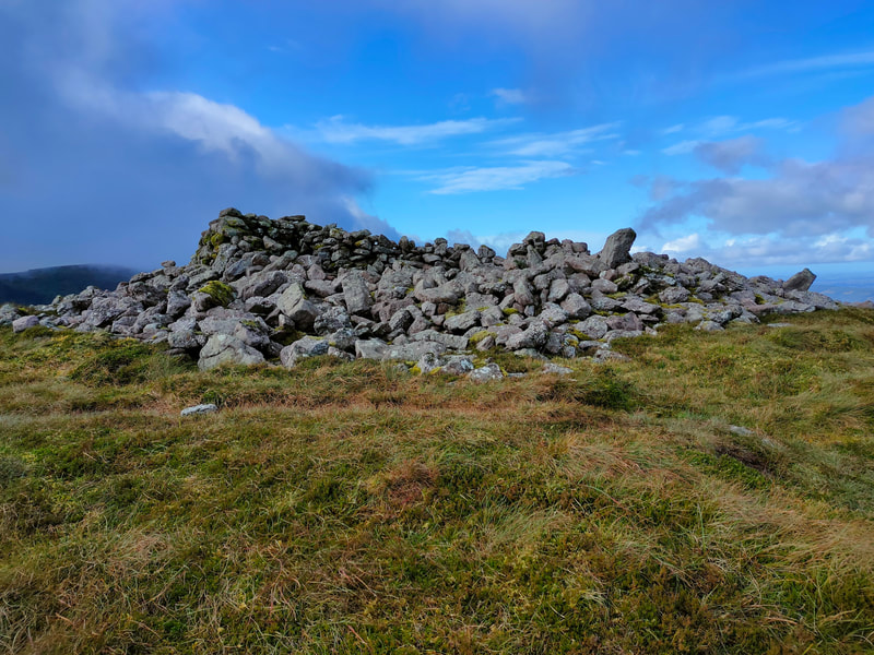 Large cairn of stones on mountain top against blue sky