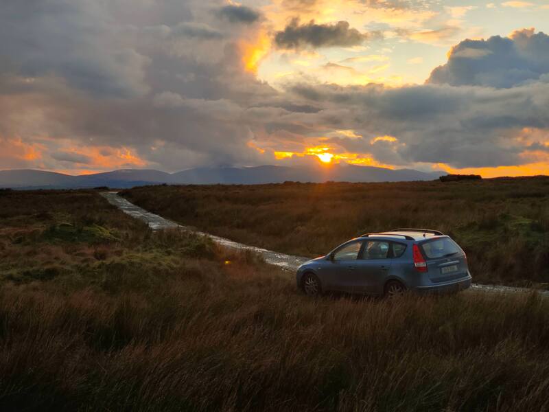 Sky after sunset with car parked on road through bog