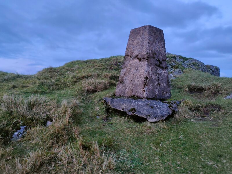 Trig Pillar on green mountain top with blue sky