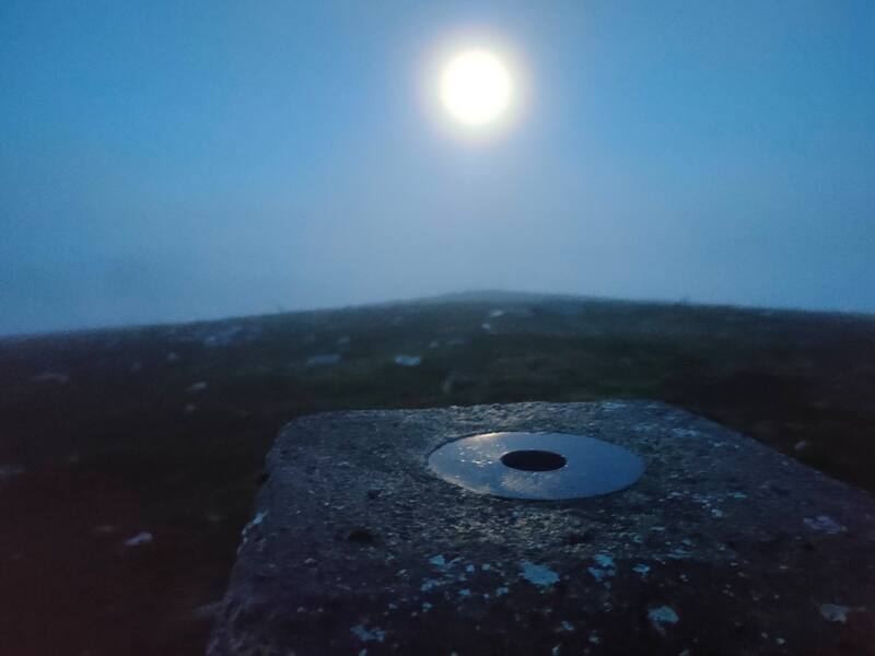 The full moon shining on the top circular plate of a trig pillar