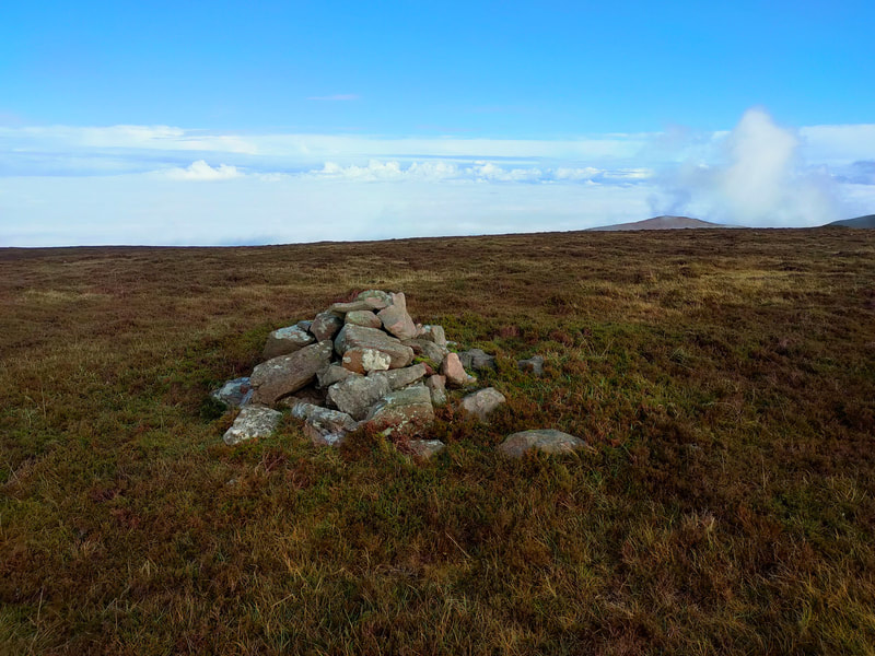 Small pile of stones on brownish heather and grass marks the top of Knocknagnauv